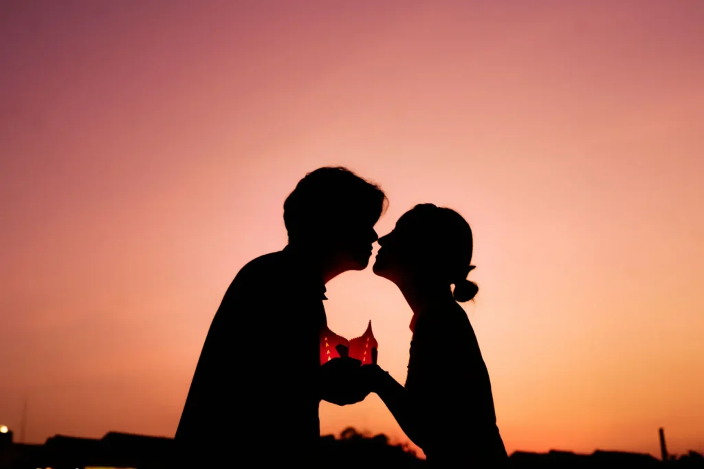 Silhouette of a couple almost kissing at sunset while holding a lit diya lamp