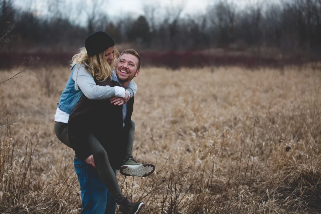 Smiling man giving a woman a piggyback ride through a golden autumn field.