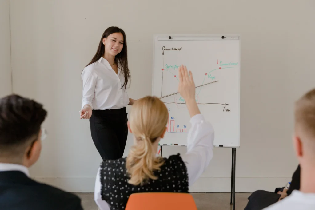 Woman presenting a commitment and satisfaction chart on a whiteboard to seated colleagues
