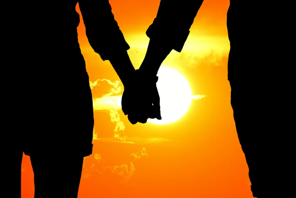 Silhouette of a couple holding hands in front of a bright orange sunset