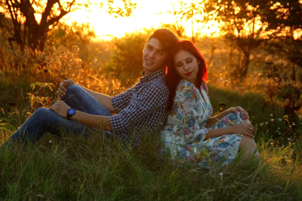 Young couple sitting back to back in a grassy field at golden sunset